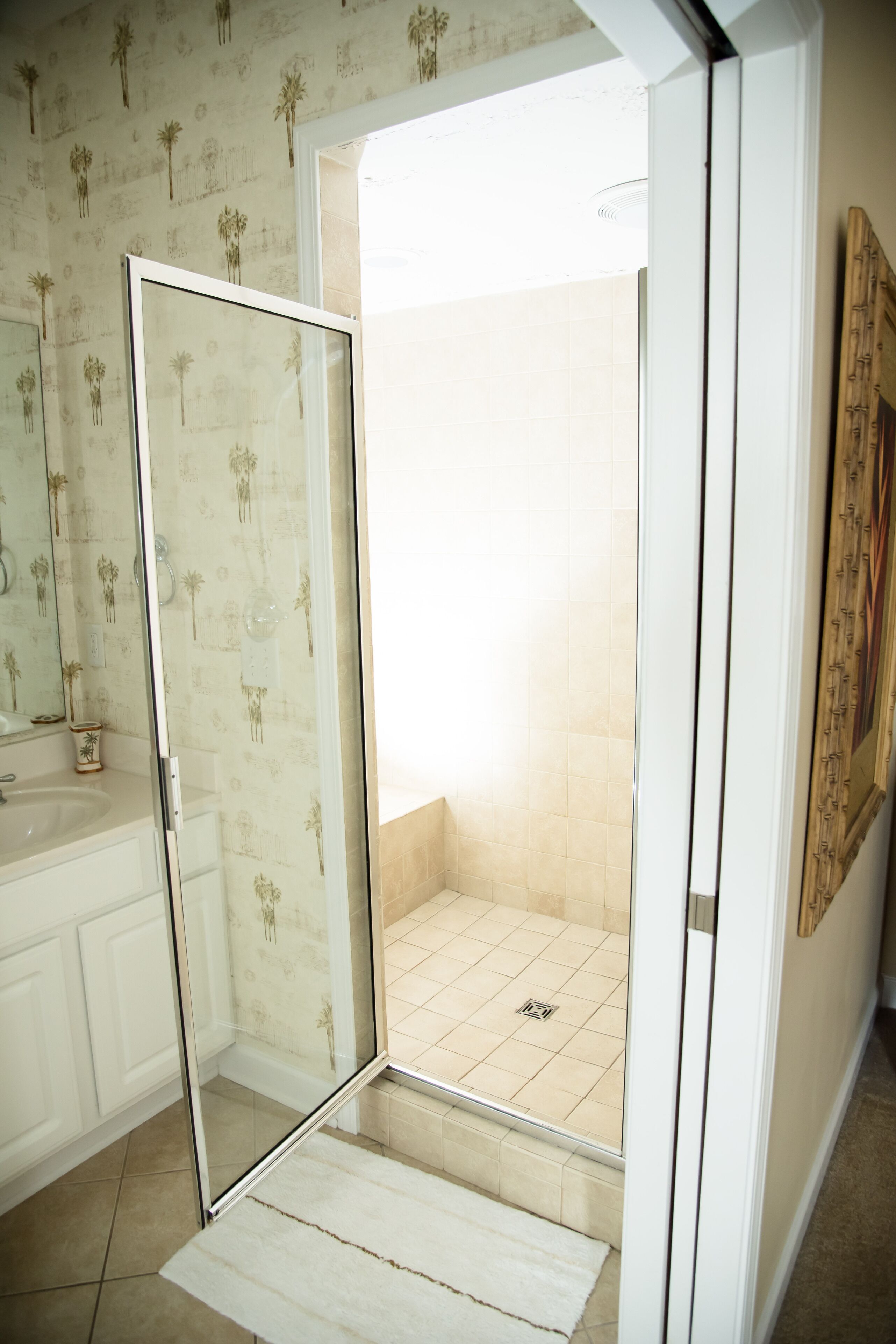 Une salle de bain avec une douche à parois de verre, un lavabo et un papier peint à motifs.