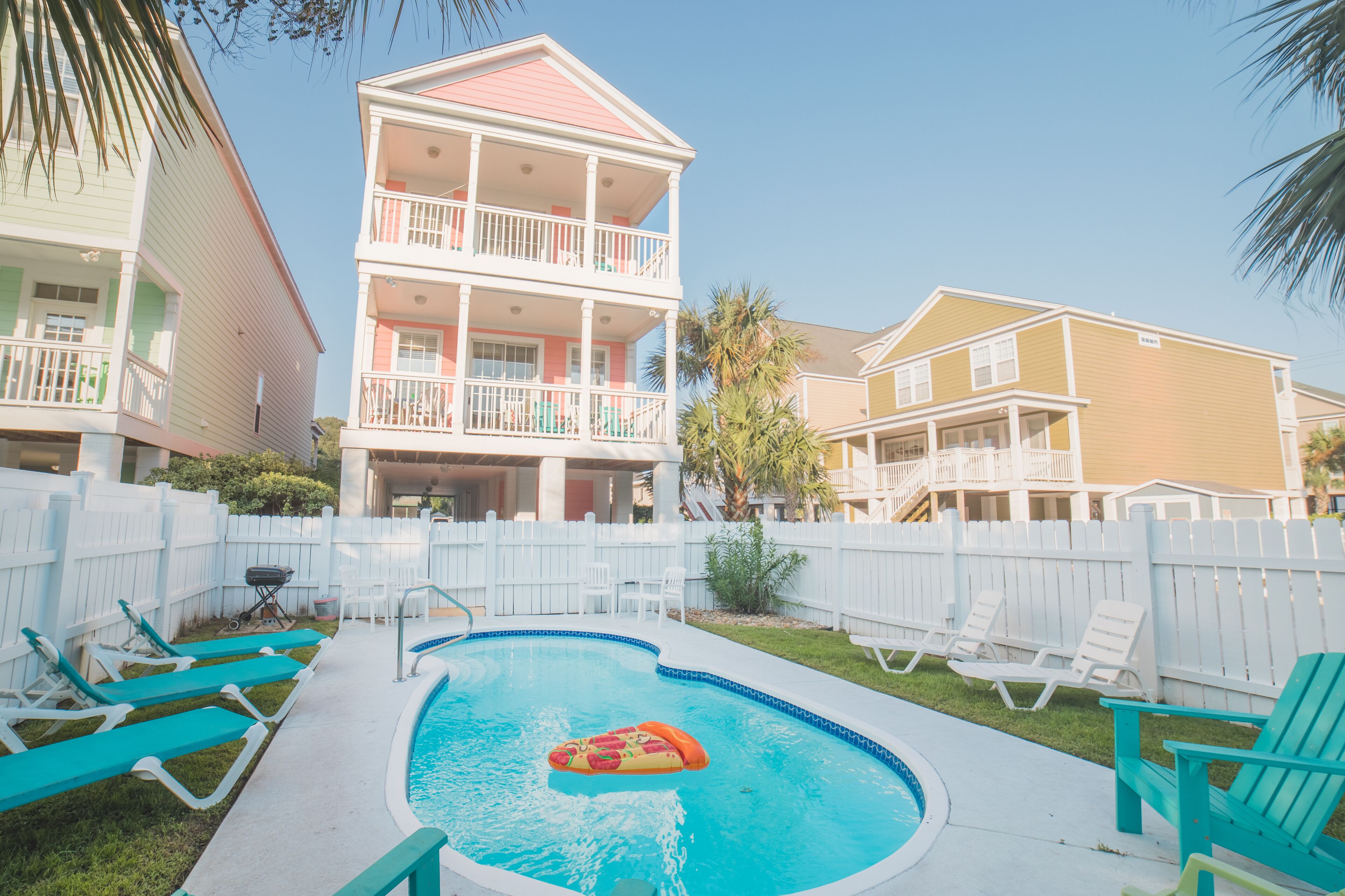 A pool area with lounge chairs, a pool, and a two-story building with balconies.