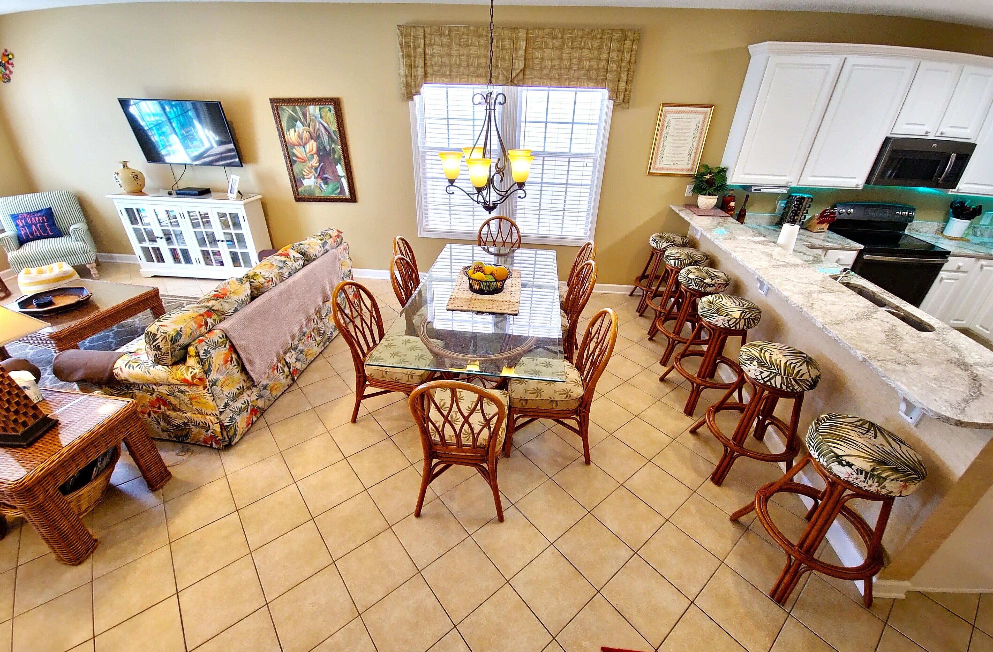 A spacious kitchen with a dining area, featuring a glass-top table, wicker chairs, and a bar with stools.