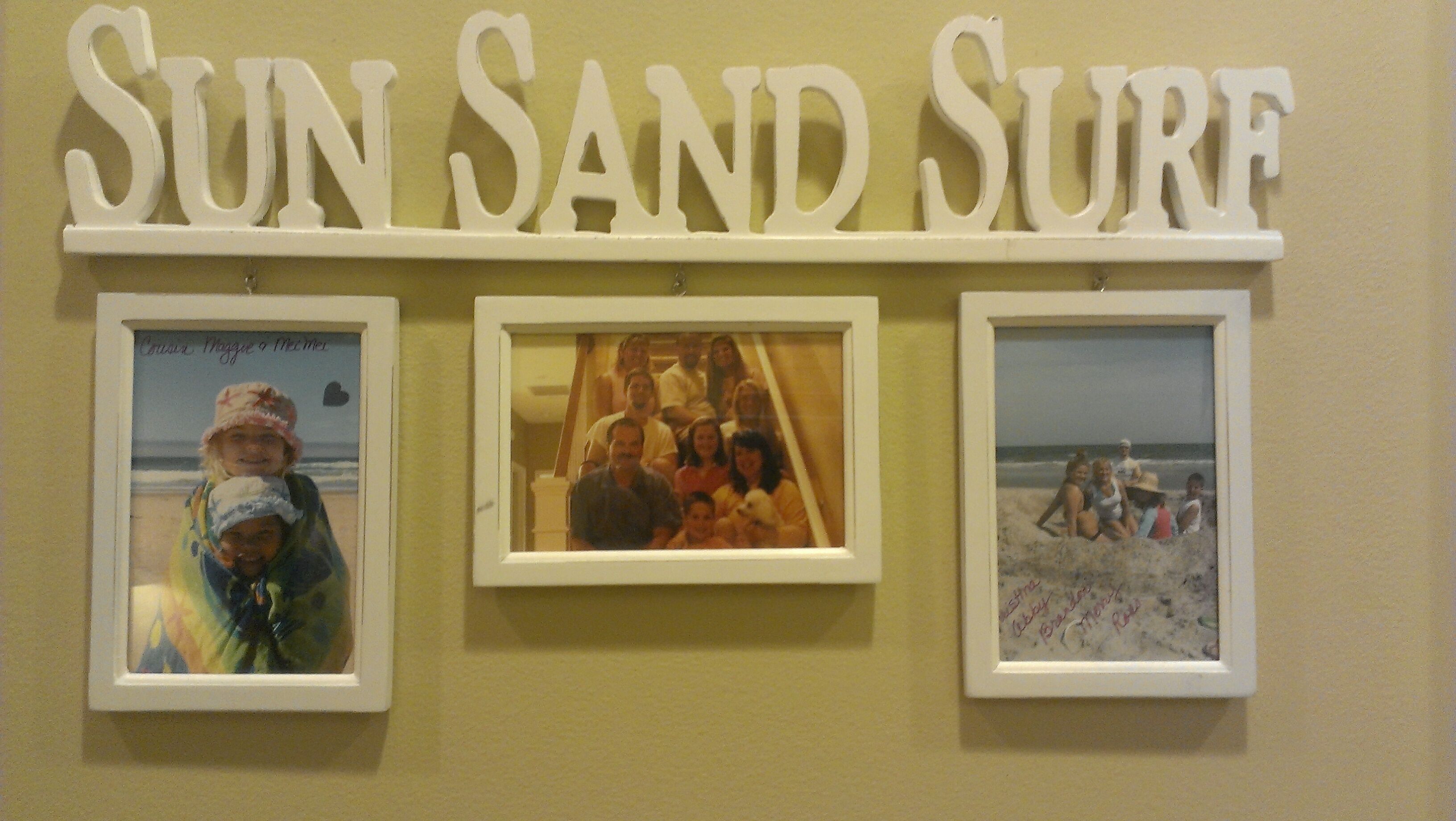 A wall with the text 'SUN SAND SURF' and three framed photographs.