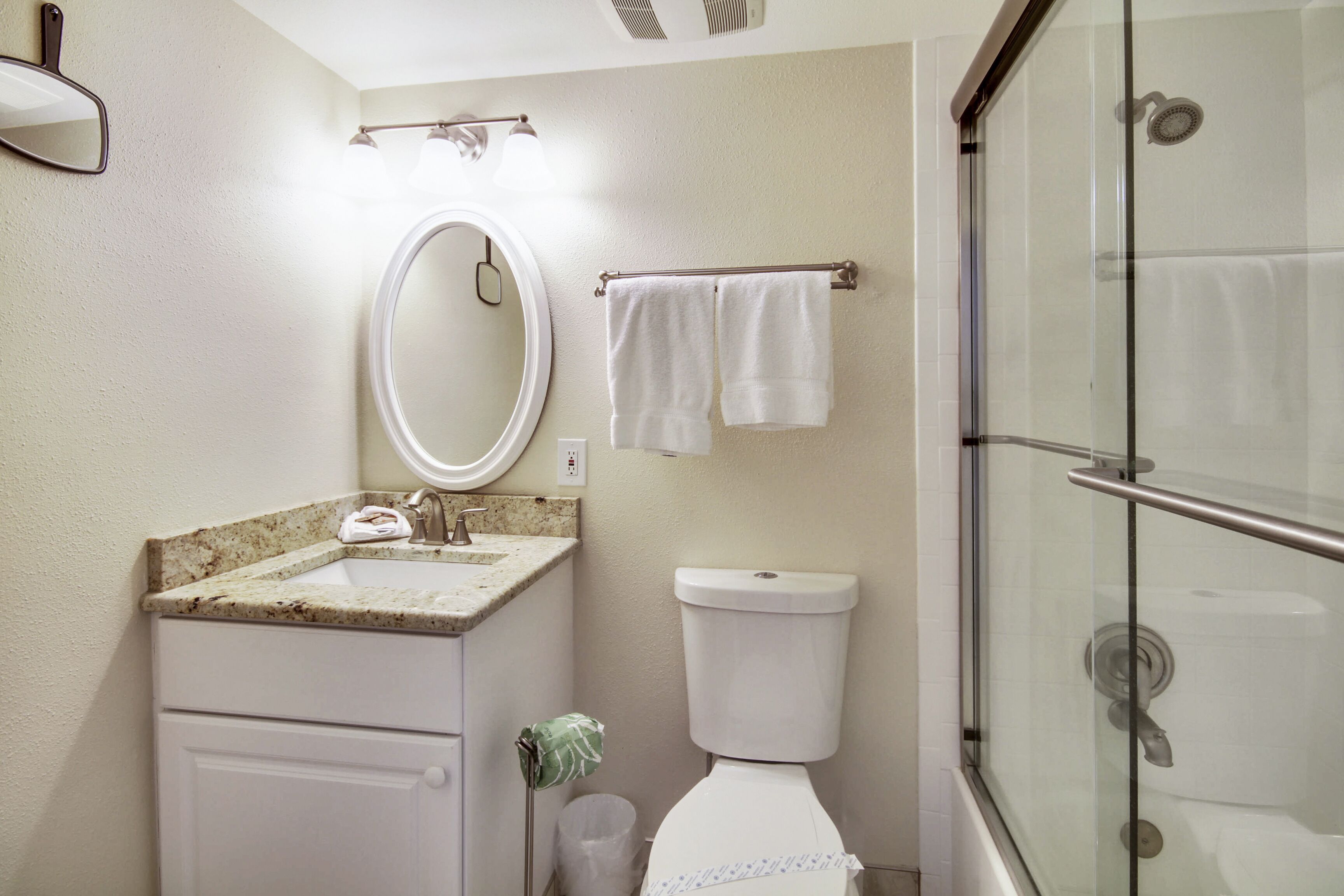 A bathroom with a sink, mirror, toilet, and glass shower enclosure.