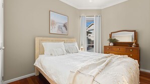 A bedroom with a wooden bed, a dresser, a mirror, and a painting on the wall. - Husky Haven by Experience Jervis Bay (Huskisson)