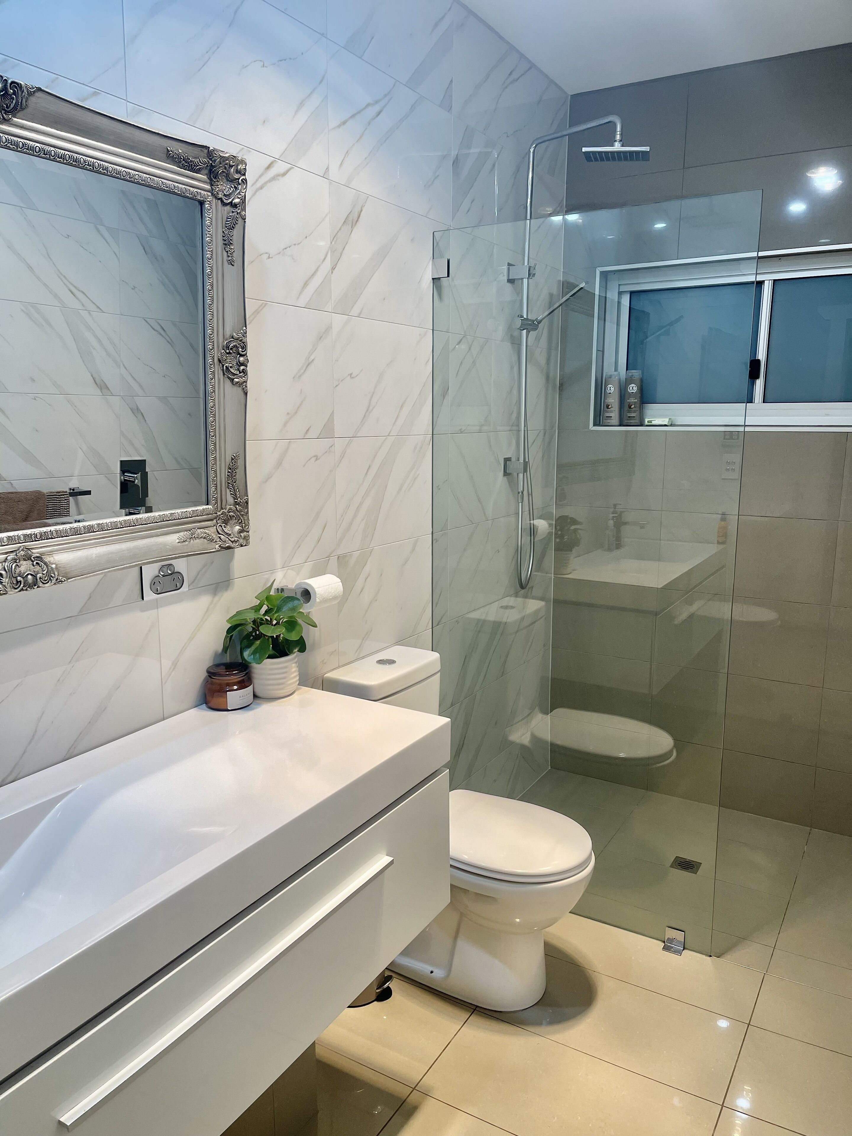 A modern bathroom with a marble-tiled wall, a white vanity, a glass-enclosed shower, and a toilet.