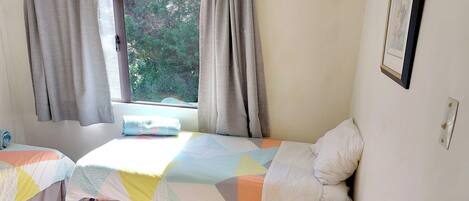 A bedroom with two beds, a window with curtains, a bedside table, and a framed picture on the wall.