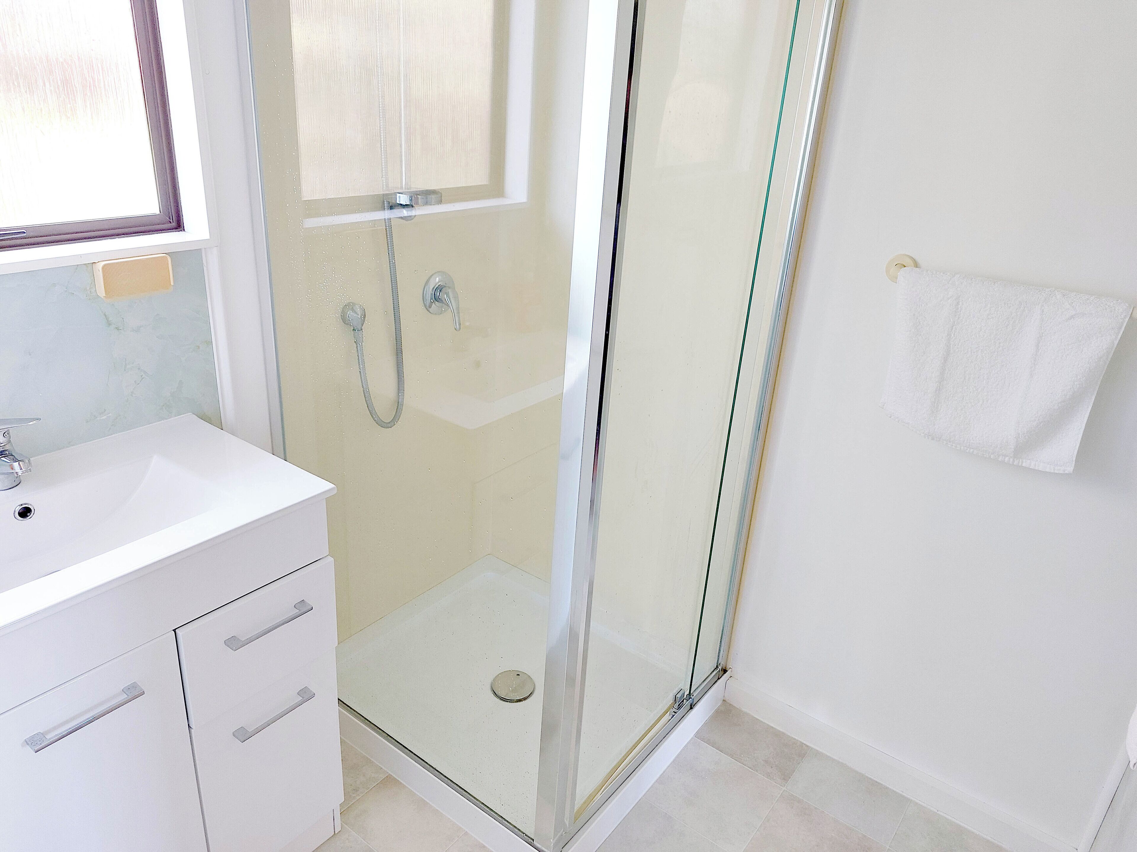 Ein modernes Badezimmer mit einer Glaskabine zur Dusche, einem weißen Waschbecken und einem Handtuch an der Wand.