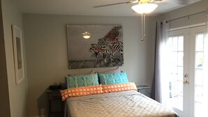 Une chambre à coucher avec un lit, un ventilateur de plafond, un tableau représentant un zèbre et une fenêtre avec des rideaux.