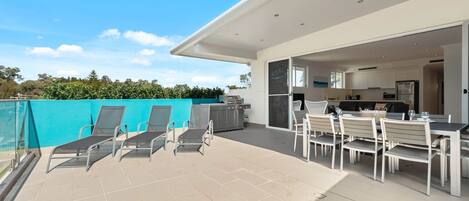 A modern outdoor patio with a dining area, a barbecue grill, and a view of the surrounding greenery.