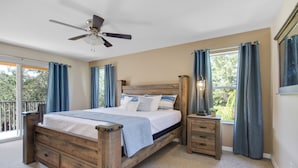 A bedroom with a wooden bed, a ceiling fan, a nightstand with a lamp, and a view of the outdoors through a window.