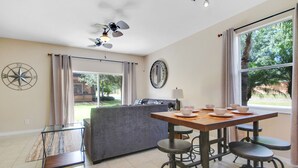 A modern kitchen with a dining area, large windows, and a ceiling fan.