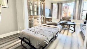 Ett modernt sovrum med en säng, en tv, en soffa och ett stort fönster med gardiner.