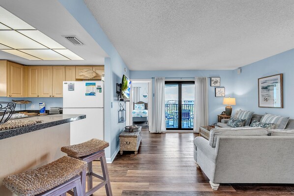 A modern kitchen with wooden cabinets, a built-in island, and a dining area with a view. - Caprice 501 Top Floor Corner|Stunning Beach Views|Walk to everything! (St. Pete Beach)