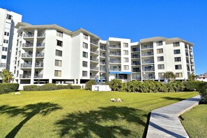 A multi-story residential building with balconies, a well-maintained lawn, and a clear blue sky.