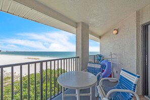 Un balcon avec vue sur la plage et l’océan, une table et une chaise bleue et blanche.