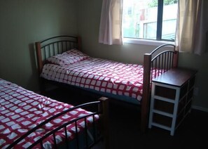 A small, single-bed room with a window, a wooden ladder, and a metal bed frame. - Kākā Point Beach House (Kaka Point)