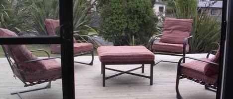 A deck with four lounge chairs and a central ottoman, surrounded by greenery.