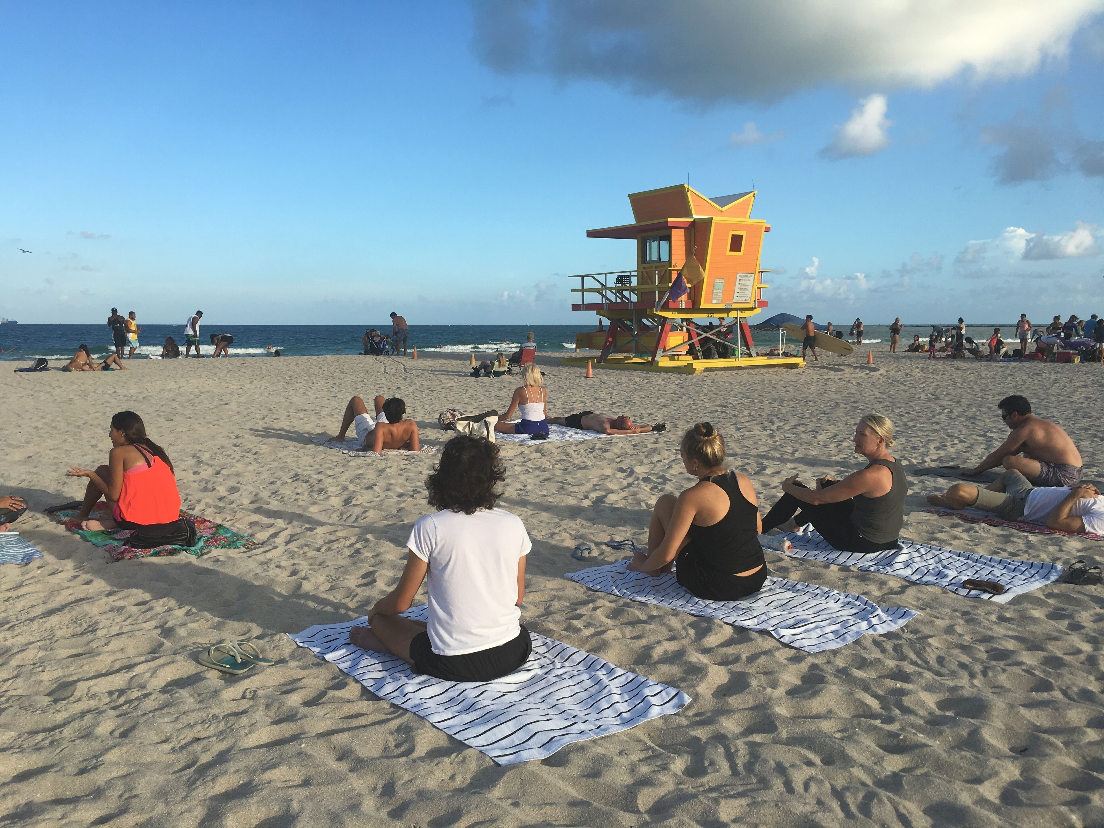 Une plage où des gens se prélassent au soleil, avec une tour de surveillance en arrière-plan.