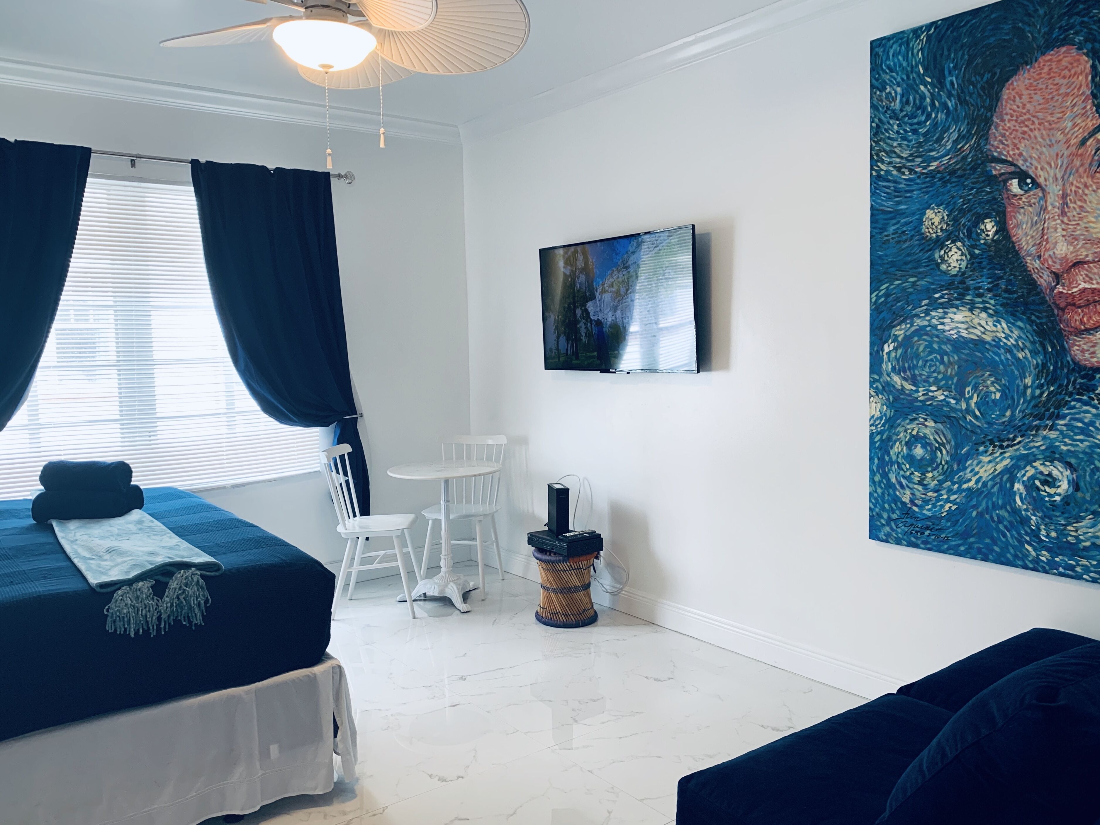 A bedroom with a bed, a TV, a painting, and a window with curtains.