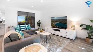 A modern living room with a sofa, a coffee table, a flat-screen TV, and a view of the sea.