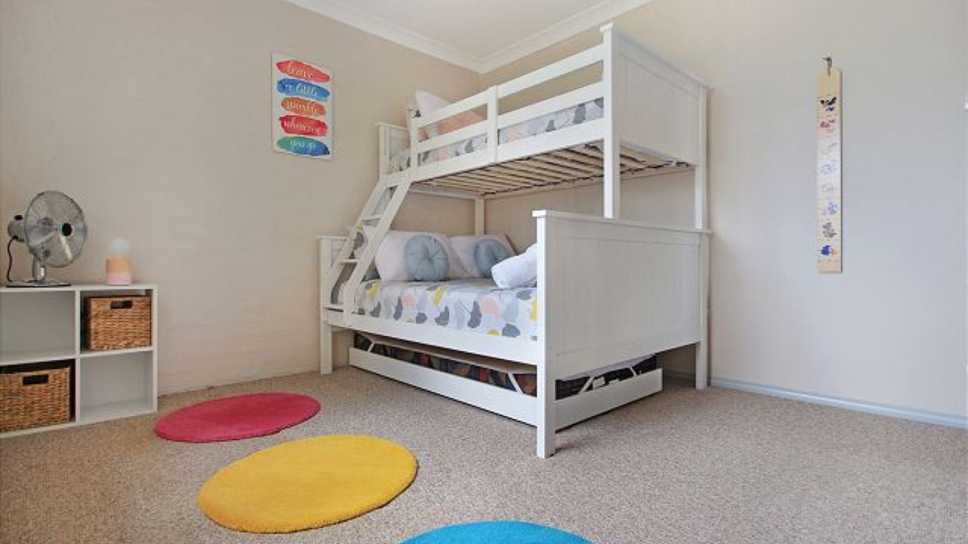 Een slaapkamer met stapelbed, een witte kleurstelling, decoratie aan de muur en een ventilator.