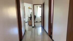 A hallway with a shiny tiled floor, wooden doors, and a small wooden cabinet with a fan and decorative items. - Casa para 05 pessoas próxima das melhores praias.... (Arraial D'Ajuda (Porto Seguro))