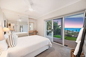 Een slaapkamer met een groot bed, een bureau en uitzicht op de oceaan door een schuifdeur.