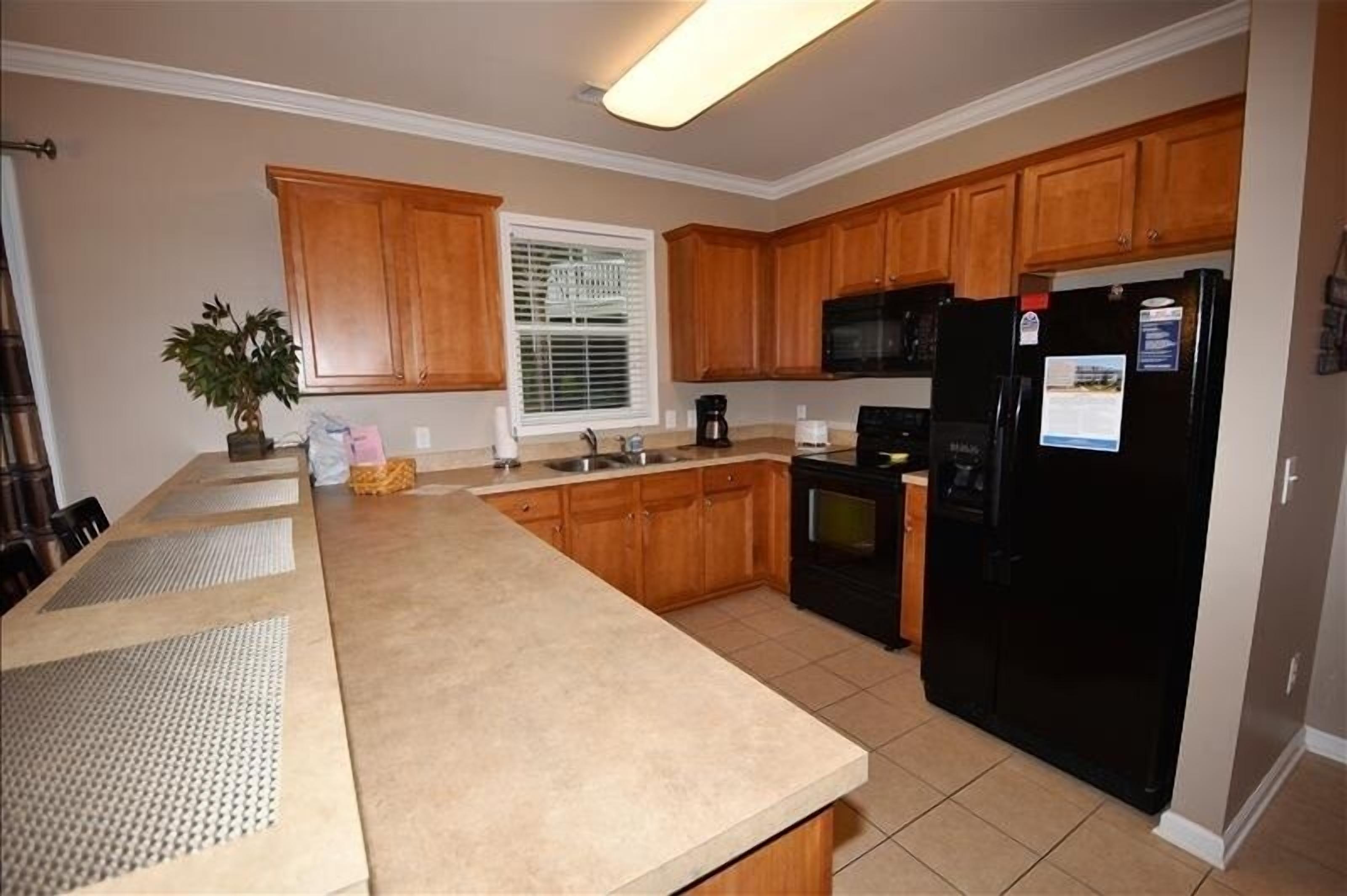 A kitchen with wooden cabinets, a black refrigerator, a microwave, and a window with blinds.