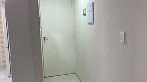 Un corridoio stretto con una porta bianca in fondo, un interruttore sulla parete e una presa elettrica.