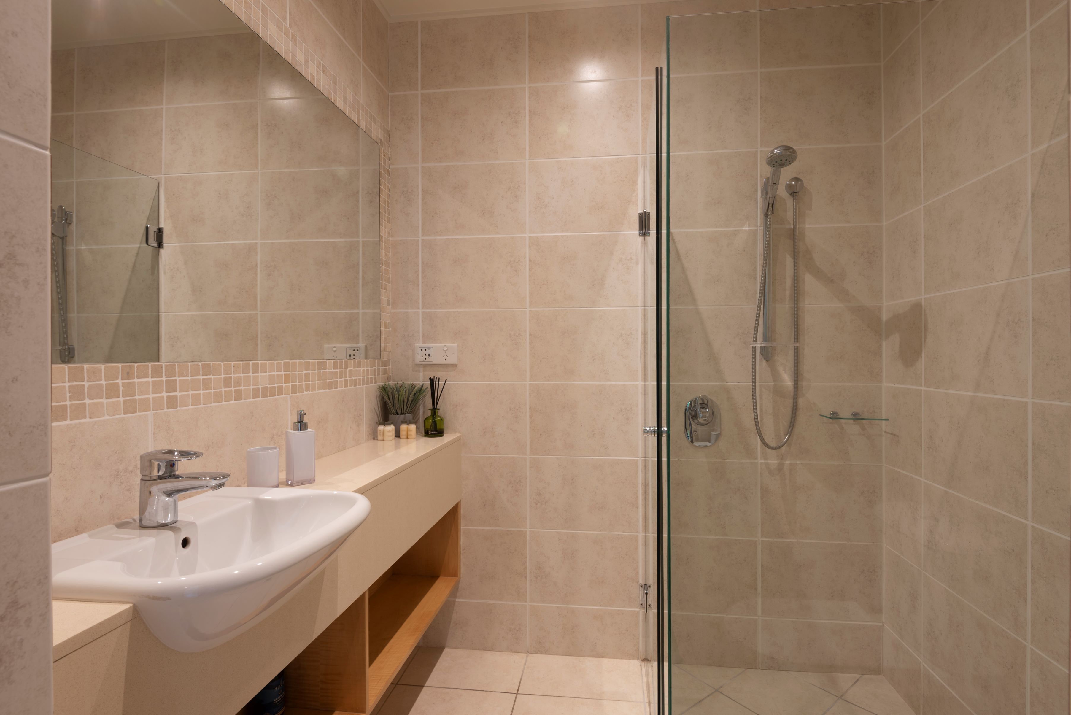 Une salle de bain moderne avec une douche à parois de verre, un lavabo avec un miroir au-dessus et un meuble-lavabo avec une étagère.