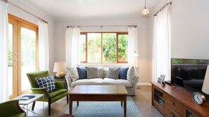 A living room with a sofa, a green armchair, a coffee table, a TV, and a lamp. - Solomon Street Cottage (Fremantle)