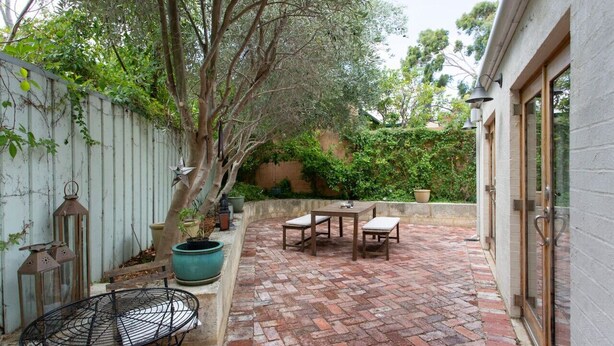 A patio area with a brick floor, a table with chairs, and a metal chair. - Solomon Street Cottage (Fremantle)