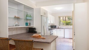 Une cuisine moderne avec des meubles blancs, un plan de travail en granit et un coin repas doté de chaises en osier.
