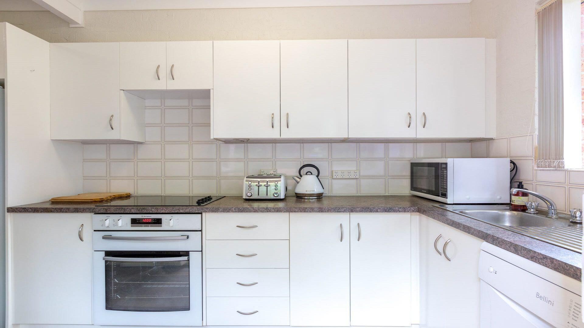 A kitchen with white cabinets, a toaster, a kettle, a microwave, and an oven.