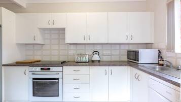 A kitchen with white cabinets, a toaster, a kettle, a microwave, and an oven.
