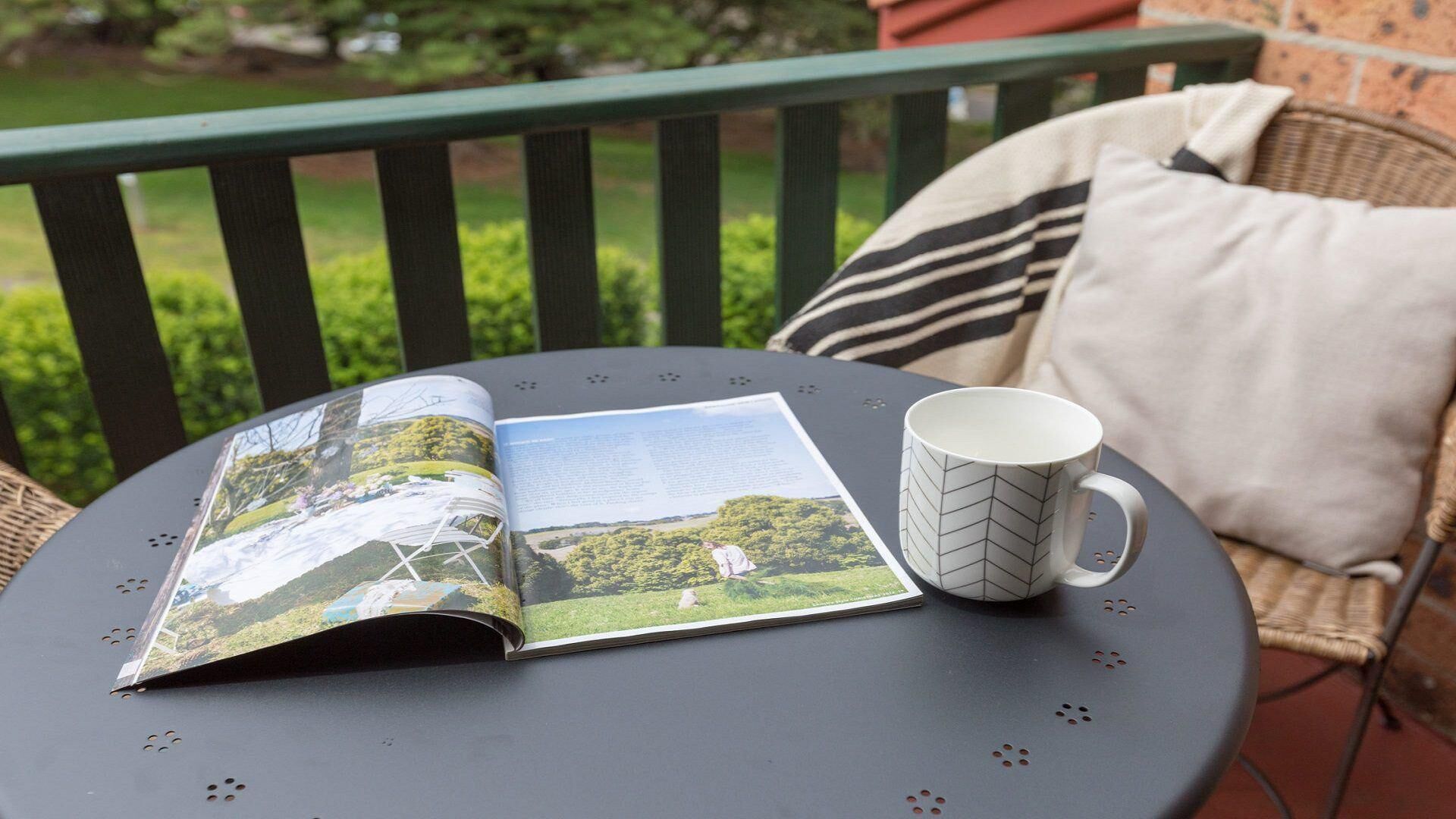 A table with a magazine, a mug, and a cushion on a balcony.
