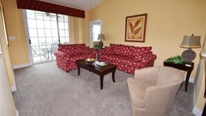 Un salón con un sofá estampado rojo, un sillón beige, una mesita de centro y una lámpara.