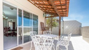 A patio with a table and chairs, a pergola, and a view of the interior through glass doors. - Penthouse by Praia do Forte In Cabo Frio (Cabo Frio)