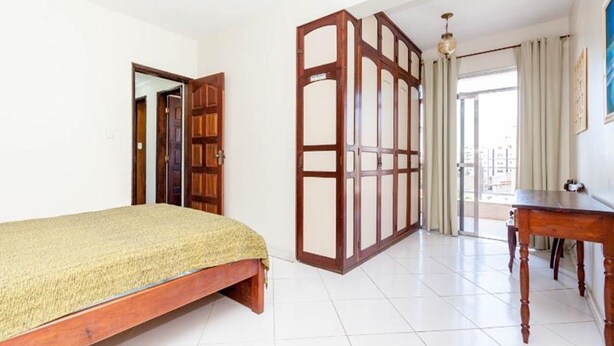 A bedroom with a bed, a wooden wardrobe, a desk, and a view of the outside. - Penthouse by Praia do Forte In Cabo Frio (Cabo Frio)