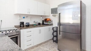 A modern kitchen with white cabinets, a stainless steel refrigerator, a gas stove, and a microwave. - Penthouse by Praia do Forte In Cabo Frio (Cabo Frio)