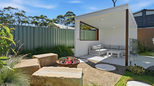 A modern outdoor living space with a fire pit, seating area, and a covered patio. - Iluka @ Wrights Beach, Jervis Bay (Wrights Beach)