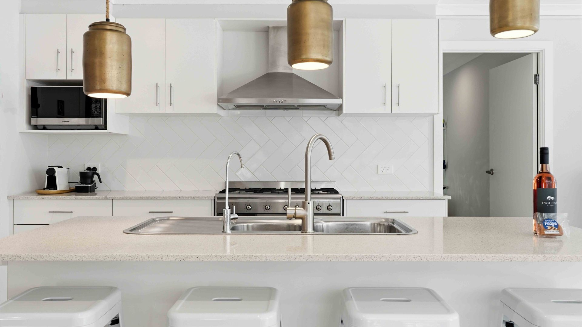 Una cocina moderna con armarios blancos, electrodomésticos de acero inoxidable, una isla central con pileta e iluminación colgante.