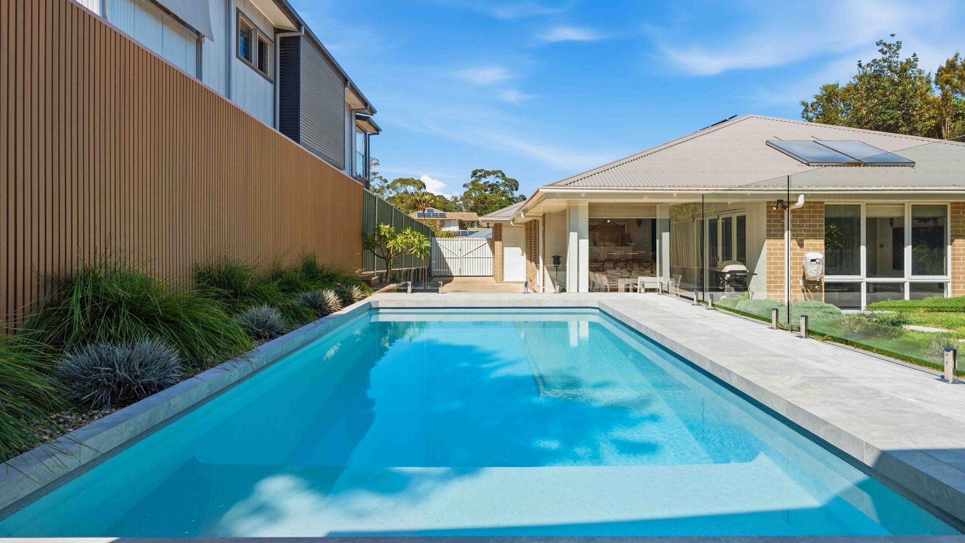 Une piscine entourée d’une clôture en bois, une maison en briques et une porte en verre.