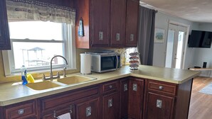 A kitchen with wooden cabinets, a microwave, a sink, and a window with a view of a patio. - 1 bed/ba lakeside cottage, large deck, west side of Seneca Lake. Pet Friendly!  (Penn Yan)