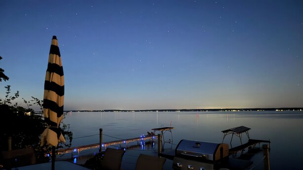A waterfront dining area with a grill, chairs, and an umbrella. - 1 bed/ba lakeside cottage, large deck, west side of Seneca Lake. Pet Friendly!  (Penn Yan)