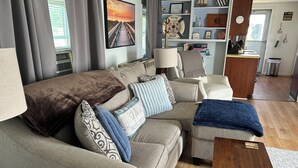 A living room with a sofa, a coffee table, a lamp, and a bookshelf. - 1 bed/ba lakeside cottage, large deck, west side of Seneca Lake. Pet Friendly!  (Penn Yan)