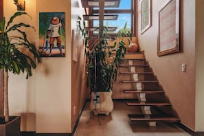 Escada com acabamento em madeira, ladeada por plantas em vasos e obras de arte.