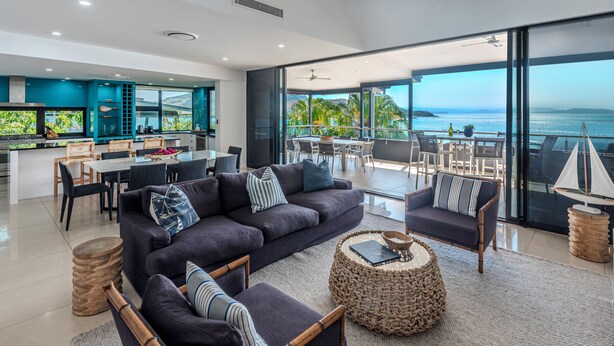 A modern living room with a large sofa, armchairs, and a dining area with a view of the ocean. - Edge 12 Hamilton Island -  absolute oceanfront with golf buggy (Hamilton Island)