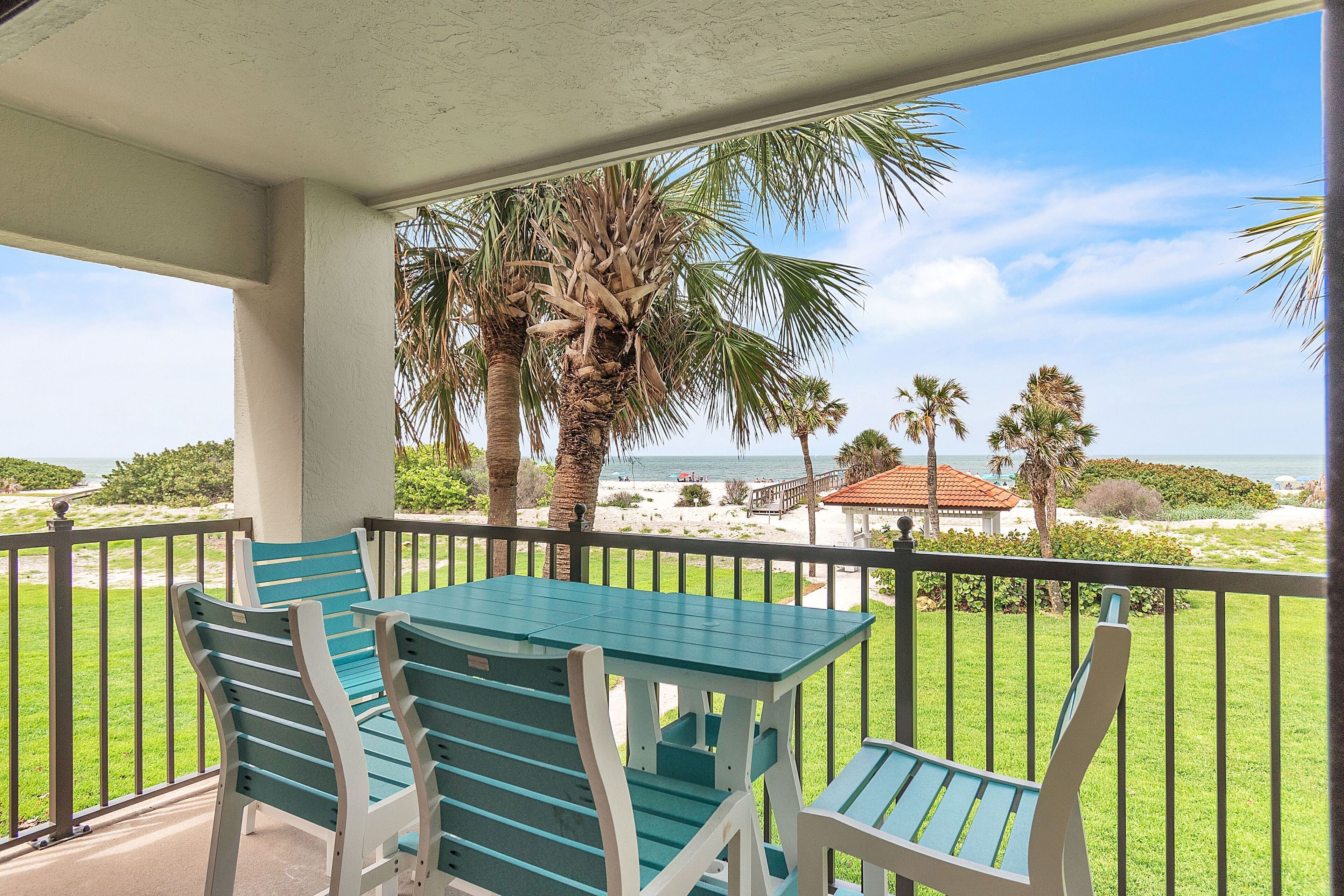 A balcony with a table and chairs, overlooking a beach with palm trees and a view of the ocean.