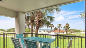 A balcony with a table and chairs, overlooking a beach with palm trees and a view of the ocean.