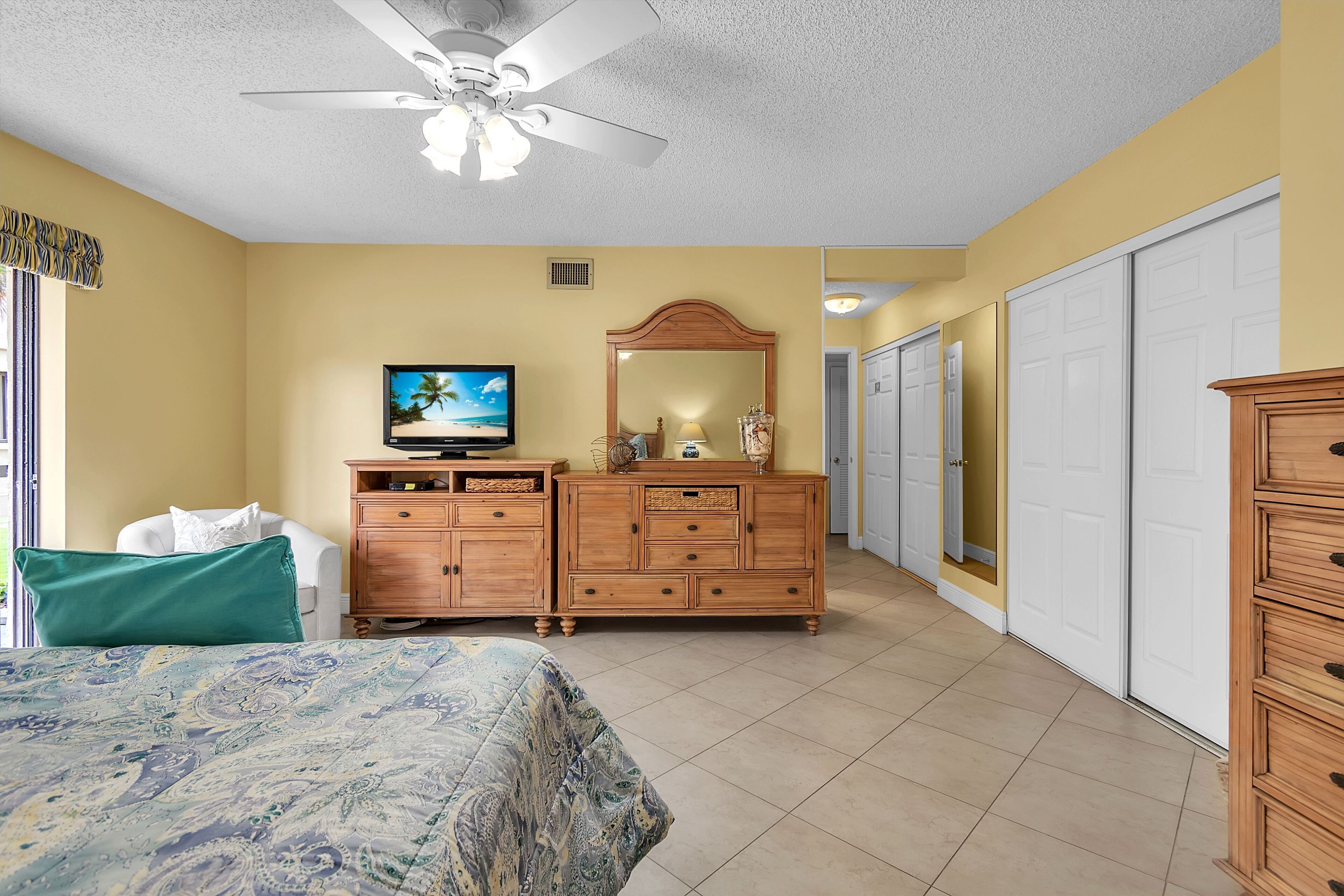 A bedroom with a bed, a dresser, a television, a ceiling fan, and a closet.