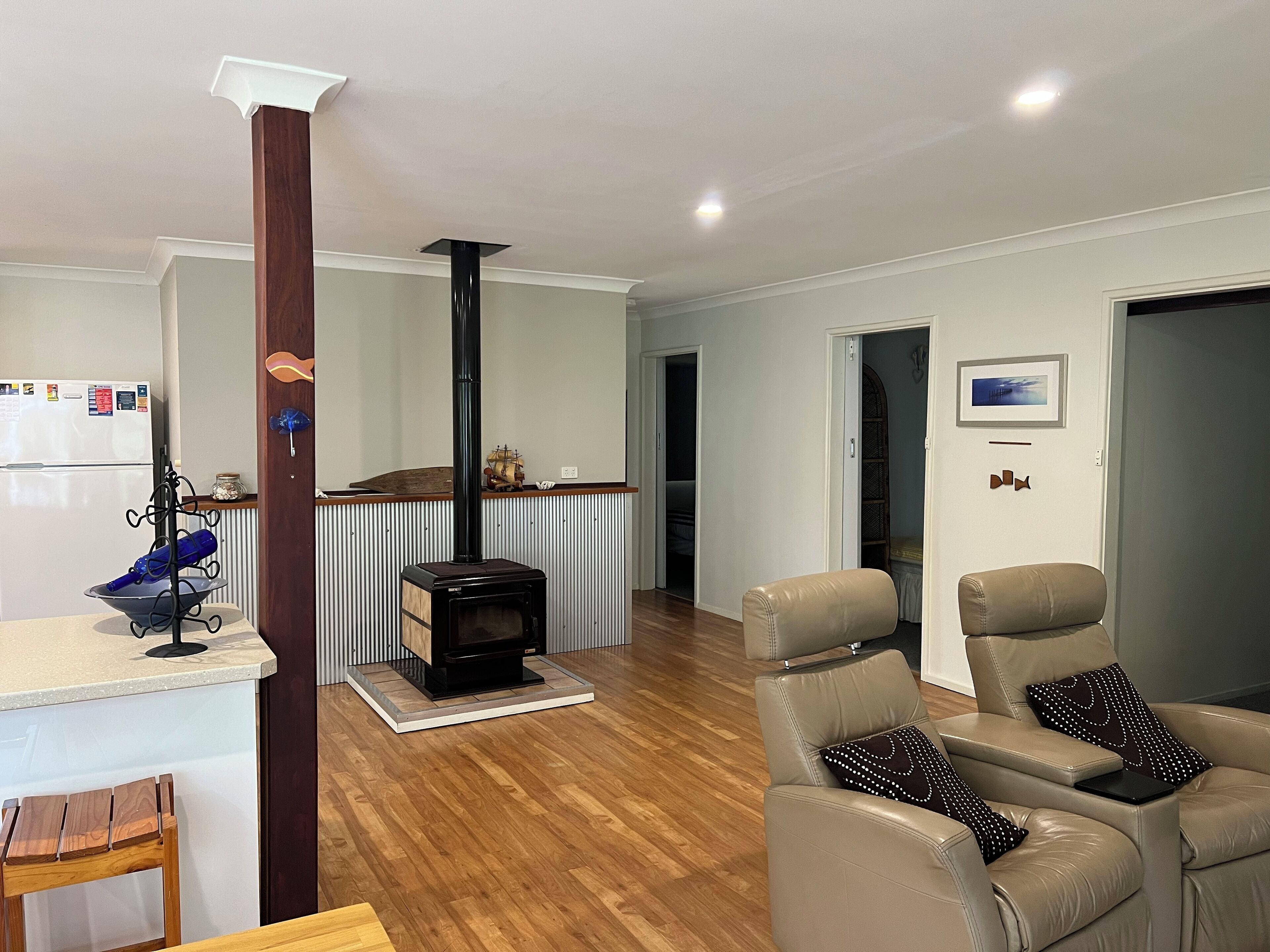 Ein modernes Wohnzimmer mit Kaminofen, Ledersofas, einem Essbereich mit Holztisch und einer Küche mit Kühlschrank.